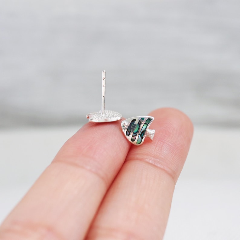 May include: A pair of silver stud earrings featuring a small, green and white fish design. The fish is made of mother-of-pearl.
