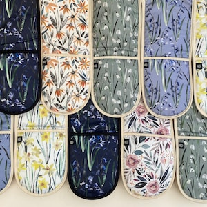 May include: Set of 10 oven mitts with floral patterns. The mitts are made of fabric with a cream background and feature different floral designs, including bluebells, daffodils, snowdrops, and wildflowers. Each mitt has a pocket on the back.