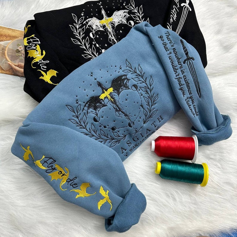 May include: Two sweatshirts with embroidered designs. One is black with a white dragon and the other is blue with a black dragon. Both have the words "Fly or die" embroidered in yellow. The blue sweatshirt also has the words "Asgiath War College" embroidered on it.