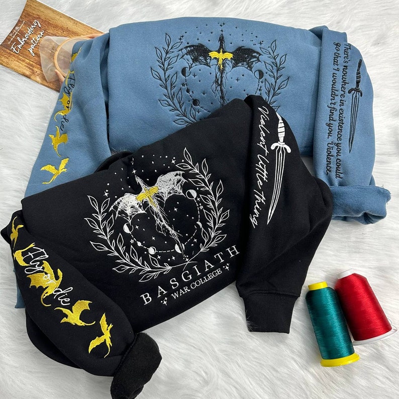 May include: Two sweatshirts with embroidered designs. One is black with a white dragon and the text "BASGIATH WAR COLLEGE +" and "Violent little thing". The other is blue with a white dragon and the text "There's nowhere in existence you could go that I wouldn't find you. "Violence"