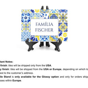 May include: A decorative tile frame with a blue, yellow, and white floral pattern. The frame features the text "FAM&Iacute;LIA FISCHER" in a central white space. It is displayed on a black stand.