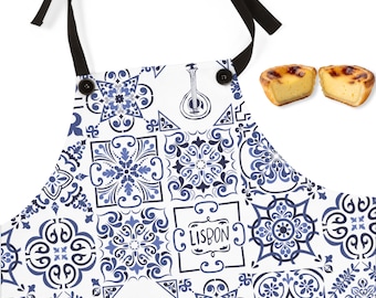 May include: White apron with a blue tile pattern and black ties. The apron features a design with the word "Lisbon" and a traditional Portuguese stringed instrument. Two custard tarts are shown next to the apron.