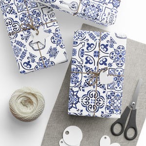 May include: Gift-wrapped boxes with blue and white patterned paper, tied with twine and blank tags. A ball of twine, scissors, and blank tags are also present. The wrapping paper has a tile-like design.
