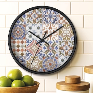 May include: A round wall clock with a black frame. The clock face features a patchwork design of colorful, patterned tiles in shades of blue, orange, and white. The clock hands are black. The clock is hanging on a white tiled wall.