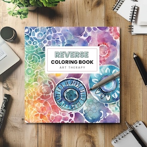 Könnte beinhalten: Ein "Reverse Coloring Book" mit einem Aquarelldesign in Blau-, Lila-, Rosa- und Grüntönen. Der Einband trägt den Text "REVERSE COLORING BOOK ART THERAPY" in einem weißen Rechteck. Ein Stift liegt auf dem Buch.