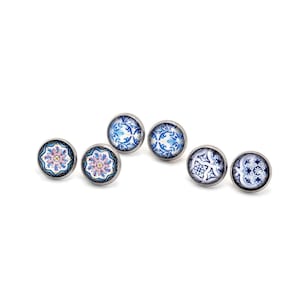 May include: Five circular stud earrings with silver-toned metal settings. Two earrings feature a central pink floral motif on a blue and white background. Three earrings display intricate blue and white geometric patterns reminiscent of ceramic tiles.