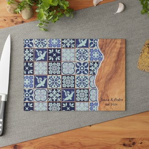 May include: A wooden cutting board with a blue and white patterned tile design. The board has a natural wood edge and is personalized with the text "Joana & Pedro Est: 2024".