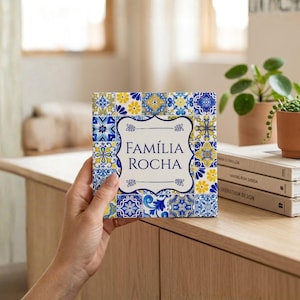 Könnte beinhalten: Quadratische Fliese mit blauem, gelbem und weißem Blumenmuster. Die Fliese hat eine weiße Mitte mit den Worten "FAMÍLIA ROCHA" in Blau. Die Fliese wird von einer Person gehalten.