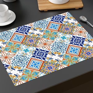 Puede incluir: Un mantel individual blanco con un patrón geométrico colorido de azulejos azules, naranjas, amarillos y verdes. El patrón recuerda a los diseños tradicionales de azulejos españoles o italianos.