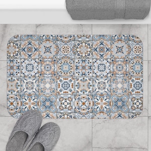 Op de afbeelding: Een blauwe en bruine badmat met een geometrisch tegelpatroon. De mat is gemaakt van zacht, absorberend materiaal en is perfect om elke badkamer een vleugje stijl te geven.