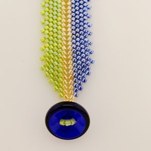 May include: A beaded bracelet with a blue, yellow, and green color scheme. The bracelet has a blue button closure.