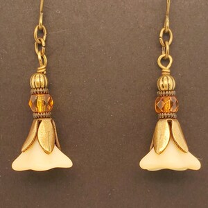 May include: A pair of gold tone earrings with a white flower charm and a brown crystal bead.