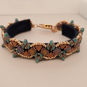May include: A beaded bracelet with a blue suede band, featuring copper and green triangular beads in a geometric pattern.