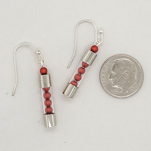 May include: A pair of silver dangle earrings with a clear tube filled with red beads.