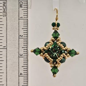 May include: A pair of green and gold dangle earrings with a square design. The earrings are approximately 2 inches long.