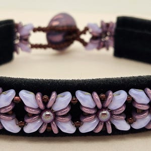 May include: A purple and brown beaded bracelet with a flower design on a black suede band.
