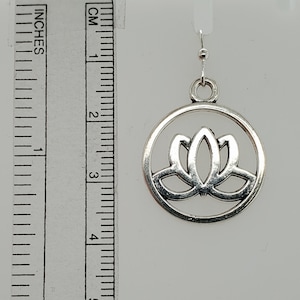 May include: Silver-toned lotus flower earring. The earring features a lotus flower design within a circular frame. The earring is approximately 1.5 inches in diameter. The earring hangs from a silver-colored fish hook.