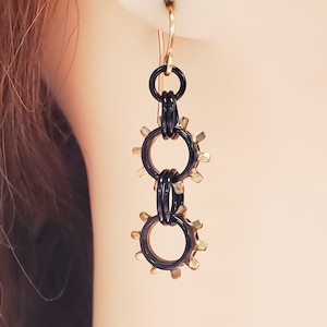 May include: Black and gold earrings with three interlocking rings and gear-shaped accents.