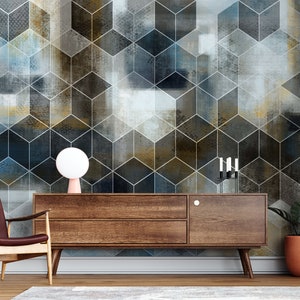 May include: A brown wooden media console with two drawers and a single door. The console is in front of a wall with a geometric pattern of blue, gray, and gold cubes. A white lamp sits on the console, and a potted plant is on the right side of the console.