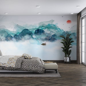 May include: A bedroom with a large wall mural depicting a blue and green watercolor mountain scene with a small boat in the water. The room has a bed with a gray and white polka dot duvet, a plant in a black pot, and a window with white blinds.