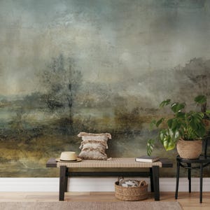 May include: A rustic, abstract landscape mural with muted green, brown, and gray tones. The mural is displayed on a wall behind a wooden bench, a straw hat, a woven pillow, and a potted plant.