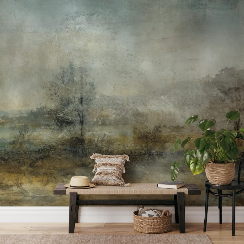 May include: A rustic, abstract landscape mural with muted green, brown, and gray tones. The mural is displayed on a wall behind a wooden bench, a straw hat, a woven pillow, and a potted plant.