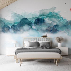 May include: A bedroom with a white bed frame and a gray duvet. The wall behind the bed has a large abstract painting of blue and green mountains with a red sun in the upper right corner.