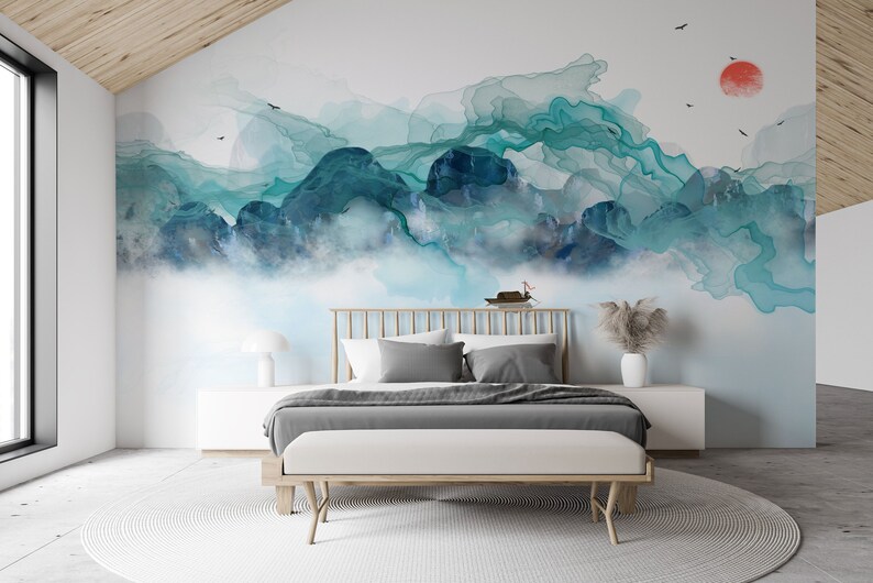 May include: A bedroom with a white bed frame and a gray duvet. The wall behind the bed has a large abstract painting of blue and green mountains with a red sun in the upper right corner.