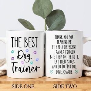 May include: White ceramic mug with the text "THE BEST Dog Trainer" on one side and a humorous message on the other. The mug features paw prints in teal, purple, and blue.