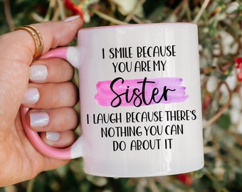 May include: A white ceramic mug with a pink handle and rim, featuring the black text I SMILE BECAUSE YOU ARE MY SISTER, I LAUGH BECAUSE THERE'S NOTHING YOU CAN DO ABOUT IT, with the word Sister highlighted by a pink watercolor brush stroke.
