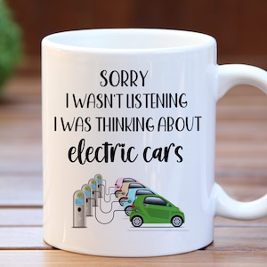 May include: White ceramic coffee mug with a black inscription that reads "Sorry I wasn't listening I was thinking about electric cars". The mug has a black and white illustration of electric cars charging at a charging station.