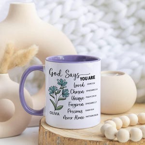 May include: White ceramic mug with a purple interior and handle. The mug features the text "God Says You Are" with a floral design and inspirational words like "Loved" and "Chosen". The mug is personalized with the name "Olivia".