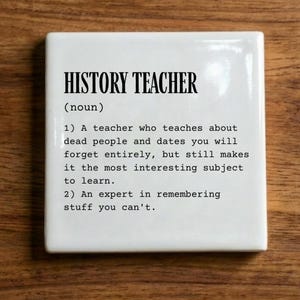 May include: A square white ceramic tile featuring black printed text that defines a history teacher as someone who teaches about dead people and dates you will forget, but makes the subject interesting, and an expert in remembering stuff you can't.