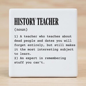 May include: A square white ceramic tile featuring black printed text that defines a history teacher as a noun. The text includes two numbered definitions describing a teacher who covers dead people and dates, and an expert in remembering facts.
