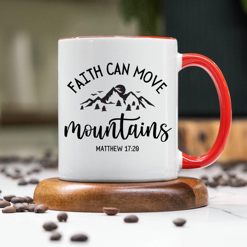 May include: A white ceramic mug with a bright red handle and interior rim. The front features black text that reads FAITH CAN MOVE mountains and MATTHEW 17:20, accompanied by a black graphic illustration of a mountain range with pine trees.