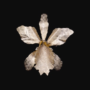 May include: A silver-colored metal orchid flower with textured petals and a yellow center, set against a black background. The flower has five distinct petals, each with a woven pattern.
