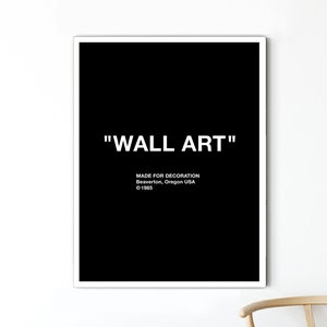 May include: A framed black and white wall art print. The print features the words "WALL ART" in white, with additional text below that reads "MADE FOR DECORATION Beaverton, Oregon USA © 1985". The print is displayed on a white wall.
