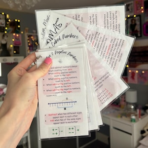 May include: A set of educational flashcards on a metal ring, with handwritten notes and diagrams about maths concepts. The cards cover topics like negative numbers, subtraction, and exponents. The text "MAS Cubed Numbers" is visible.