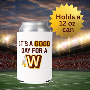 May include: White can cooler with the text "IT'S A GOOD DAY FOR A W" in maroon and gold. The cooler features a gold and maroon "W" logo with feathers. A gold starburst graphic reads "Holds a 12 oz can".