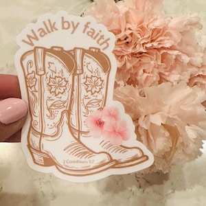 May include: A sticker featuring a pair of tan cowboy boots with floral accents and the text "Walk by faith" above the boots. The scripture reference "2 Corinthians 5:7" is below the boots. Pink flowers are next to the sticker.