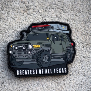 May include: A black and green illustrated patch of a Toyota FJ Cruiser with a roof top tent. The vehicle is on a white background with the text "Greatest of All Texas" below the vehicle.
