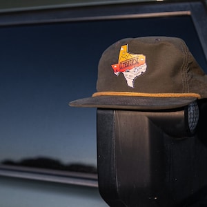May include: A green and brown baseball cap with a patch of the state of Texas that says "Greatest of All Texas".
