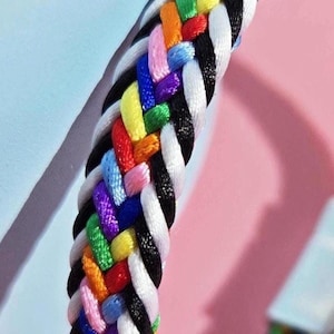 Puede incluir: Un brazalete trenzado de colores con un cierre magnético plateado. El brazalete está hecho de múltiples hilos de colores tejidos juntos en un patrón trenzado.
