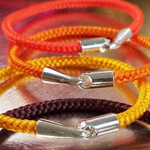 May include: Three braided rope bracelets in orange, yellow, and brown with silver clasps.