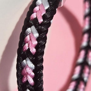 May include: A black braided bracelet with pink and white accents and a silver clasp.