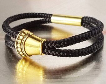 May include: A black braided cord bracelet with a gold-toned cone-shaped bead. The bracelet has a gold-toned metal clasp.