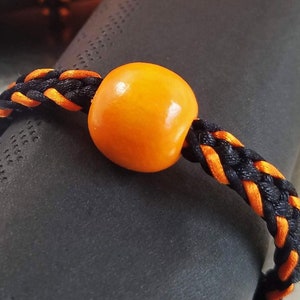 May include: Black and orange braided cord with an orange wooden bead. The cord is wrapped around a black napkin.