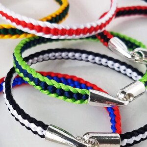 Op de afbeelding: Close-up van verschillende gevlochten armbanden in diverse kleuren, waaronder rood, wit, blauw, groen en zwart. Elke armband heeft een zilverkleurige sluiting. De armbanden zijn gerangschikt op een witte ondergrond.