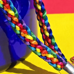 Op de afbeelding: Een regenboog gevlochten koord met een zilveren draaibare sluiting. Het koord is gemaakt van kleurrijk geweven koord en is perfect voor het dragen van sleutels, badges of andere kleine voorwerpen.