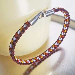 May include: A braided bracelet with red, white, and gold threads. The bracelet has a silver clasp.